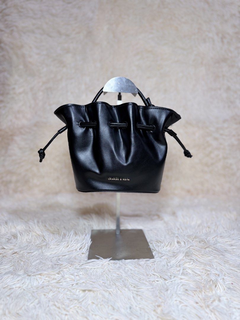 Charles & Keith Black Bucket Bag (Category: Cross-body Bags) located in Caloocan City. Submitted by hirahira.co (Listing ID 1467279573, Image 1). Description: - Brand: Charles & Keith - Color: Classic Black - Material: Soft faux leather - Closure: Drawstring top with stylish knotted side details - Handles: Small top handle + includes wrapped detachable strap - Condition: Brand new, clean structure, still stuffed with original packing paper - Perf