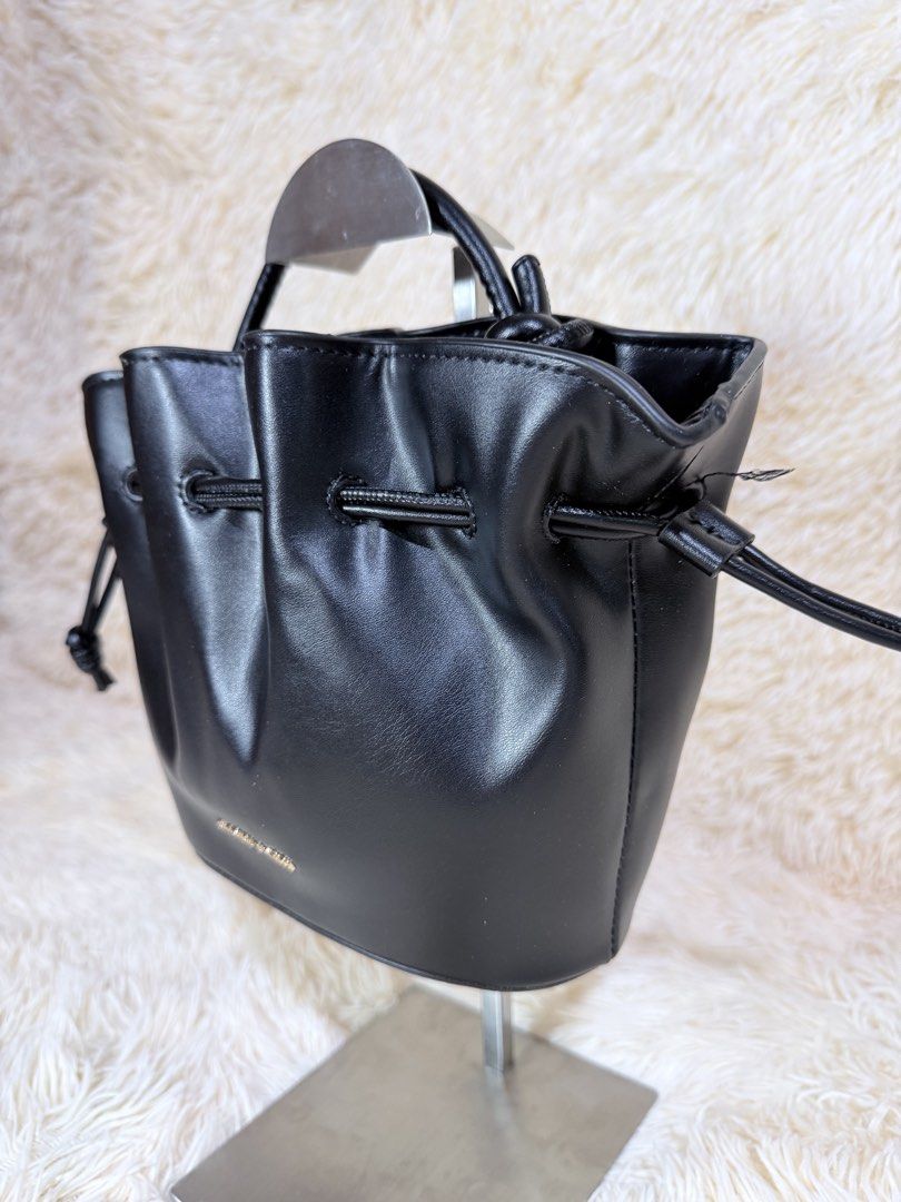 Charles & Keith Black Bucket Bag (Category: Cross-body Bags) located in Caloocan City. Submitted by hirahira.co (Listing ID 1467279573, Image 2). Description: - Brand: Charles & Keith - Color: Classic Black - Material: Soft faux leather - Closure: Drawstring top with stylish knotted side details - Handles: Small top handle + includes wrapped detachable strap - Condition: Brand new, clean structure, still stuffed with original packing paper - Perf