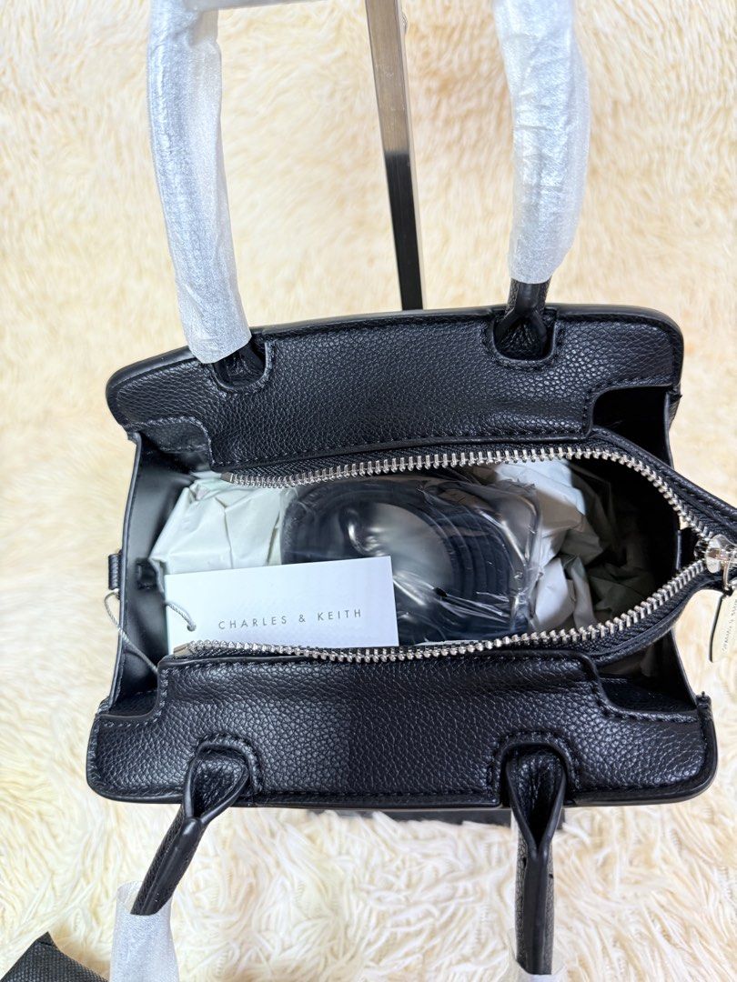 Charles & Keith Black Handbag (Category: Luxury Bags & Wallets) located in Caloocan City. Submitted by hirahira.co (Listing ID 1467279027, Image 2). Description: - Brand: Charles & Keith - Color: Classic Black - Material: Premium textured faux leather - Design: Structured trapezoid shape with vertical strap accents and silver-tone logo lettering - Closure: Top zip closure - Handles: Twin top handles (protective wrapping still intact) - Condition: