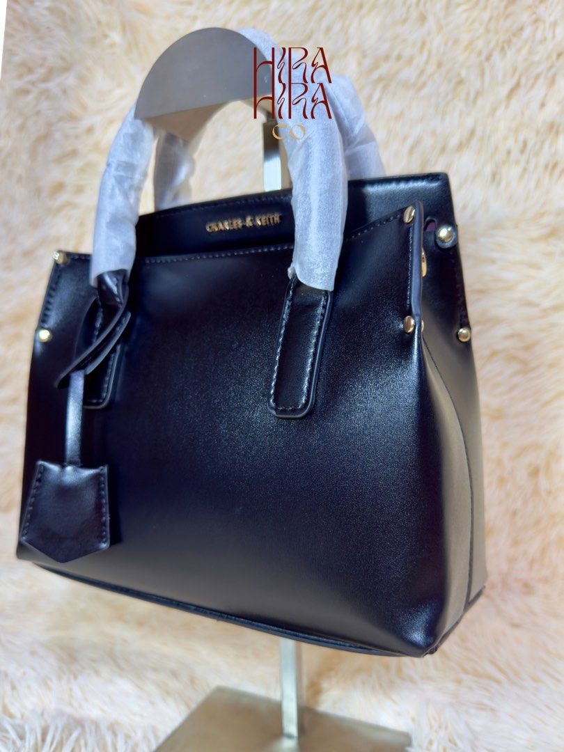 Charles & Keith Black Tote Bag (Category: Tote Bags) located in Caloocan City. Submitted by hirahira.co (Listing ID 1467283265, Image 2). Description: - Brand: Charles & Keith - Color: Classic black with sleek gold-tone side hardware - Design: Structured compact everyday bag with a clean, smooth finish - Handles: Dual top handles (still wrapped in protective paper) - Details: Includes an attached front dangling key charm - Condition: Brand new an