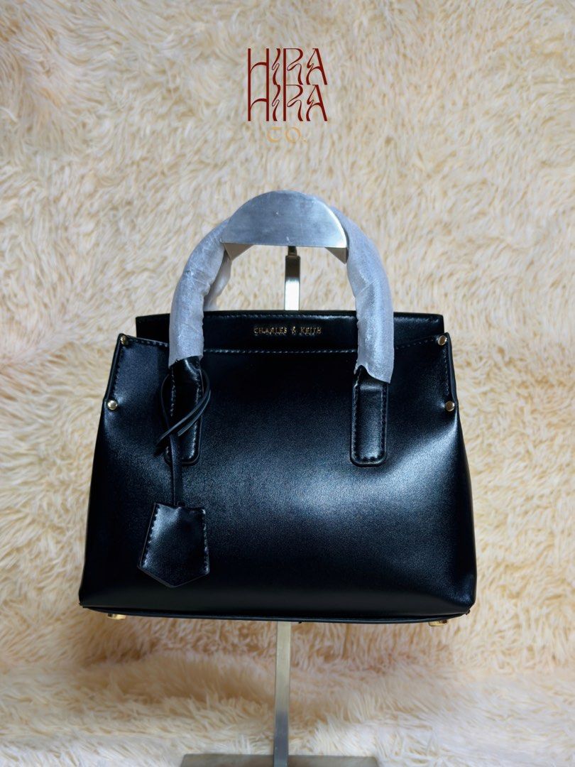 Charles & Keith Black Tote Bag (Category: Tote Bags) located in Caloocan City. Submitted by hirahira.co (Listing ID 1467283265, Image 1). Description: - Brand: Charles & Keith - Color: Classic black with sleek gold-tone side hardware - Design: Structured compact everyday bag with a clean, smooth finish - Handles: Dual top handles (still wrapped in protective paper) - Details: Includes an attached front dangling key charm - Condition: Brand new an