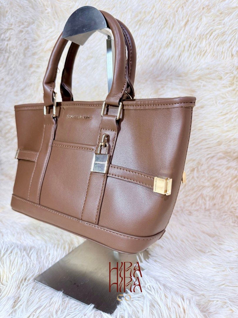 Charles & Keith Brown Handbag with Padlock (Category: Luxury Bags & Wallets) located in Caloocan City. Submitted by hirahira.co (Listing ID 1467284205, Image 2). Description: - Brand: Charles & Keith - Material: Brown faux leather - Hardware: Gold-tone - Features: Dual top handles, decorative front padlock, structured shape with flat base and protective metal feet - Condition: Clean interior and exterior - Style: Versatile neutral shade, perfect 