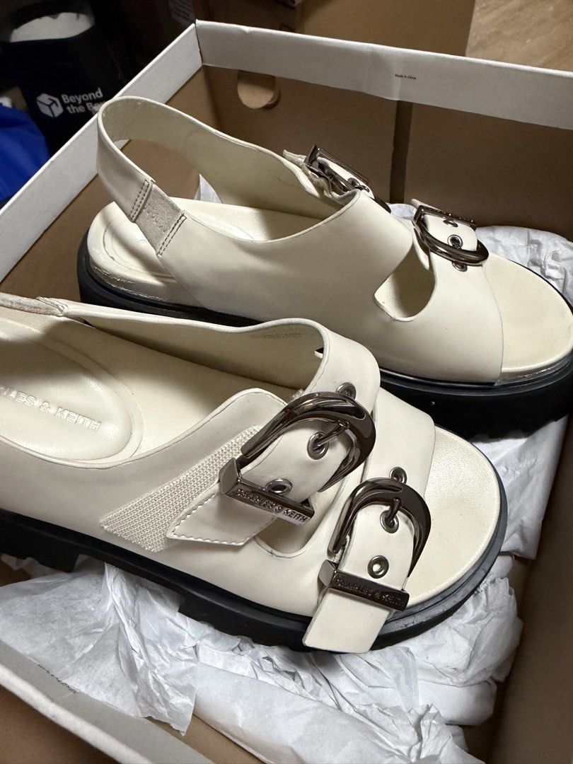 Charles & Keith White Chunky Buckle Sandals (Category: Flats & Sandals) located in Manila. Submitted by mamoru.sh (Listing ID 1467297859, Image 2). Description: - Brand: Charles & Keith - Style: White chunky sandals with double strap design - Features: Large metallic buckles, slingback strap with elastic gore, and thick black platform sole - Condition: Like New (with box) - Inclusions: Original box included - Perfect for elevating your everyday c