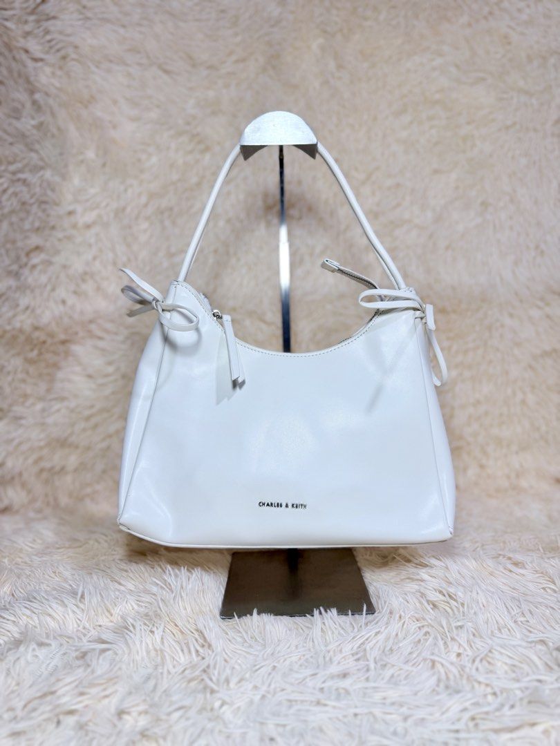 Charles & Keith White Shoulder Bag (Category: Shoulder Bags) located in Caloocan City. Submitted by hirahira.co (Listing ID 1467284521, Image 1). Description: - Brand: Charles & Keith - Color: Classic White - Design: Clean minimalist style with cute side ribbon accents - Closure: Secure zippered main compartment - Hardware: Premium metallic details with silver brand lettering - Material: Smooth, high-quality synthetic leather - Size: Practical ev