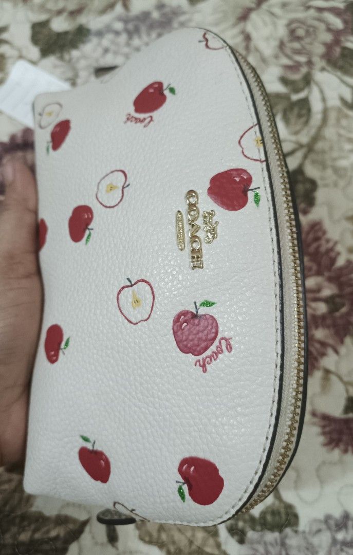 Coach White Apple Print Cosmetic Pouch (Category: Purses & Pouches) located in Capas. Submitted by rayapretty55453 (Listing ID 1467358333, Image 1). Description: Coach cosmetic pouch in white pebble leather. Printed red and sliced apple pattern all over. Gold tone hardware and zipper closure. Brown leather interior lining. Gold Coach logo embossed on the front. Good for daily use. .