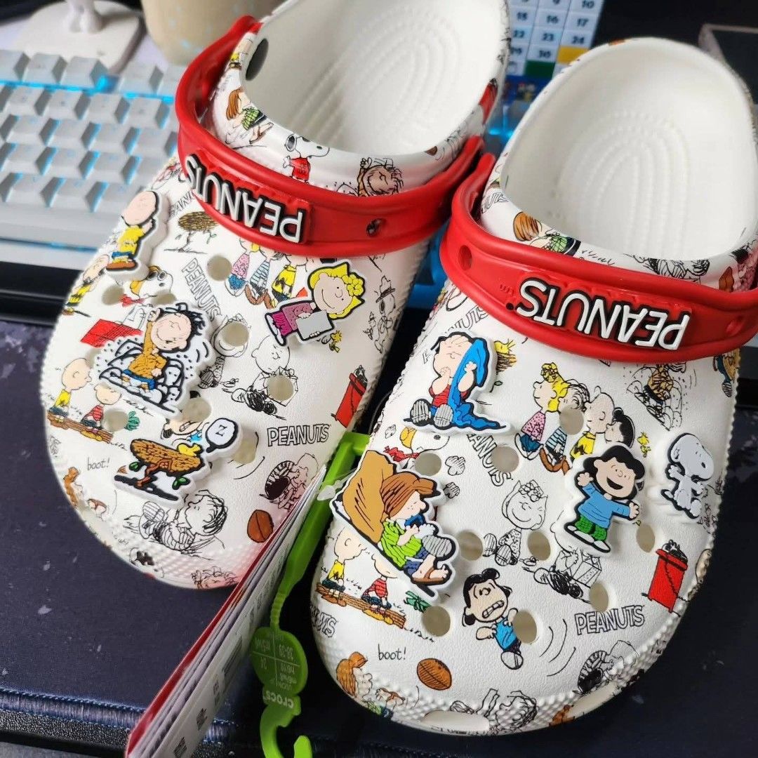 Crocs Peanuts Snoopy Charlie Brown White Clogs (Category: Slippers & Slides) located in Manila. Submitted by onlineshopmate (Listing ID 1467177656, Image 2). Description: - Brand new with green tag attached - Authentic Crocs covered in classic Peanuts comic strip prints (Snoopy, Charlie Brown & gang) - Features a contrasting red heel strap with raised 'PEANUTS' text in white - Comes with multiple character Jibbitz charms already attached - Super 