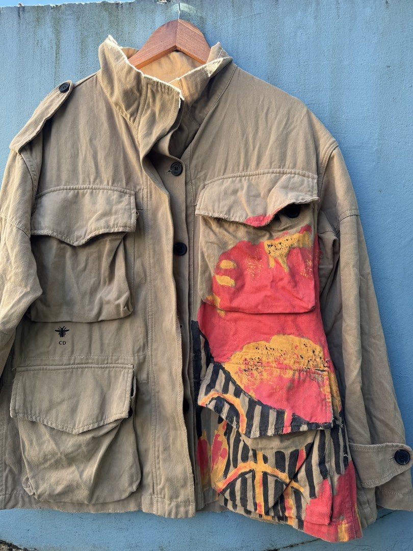 Dior Bee Painted Military Jacket (Category: Coats, Jackets and Outerwear) located in Baguio. Submitted by luxurysales2600 (Listing ID 1467175956, Image 3). Description: Khaki military style jacket with multiple utility pockets. Hand-painted floral and geometric artwork in red, yellow, black, and green across the front and back. Features the signature Dior bee embroidery above the lower right pocket. Button-up closure with stand collar and shoulde