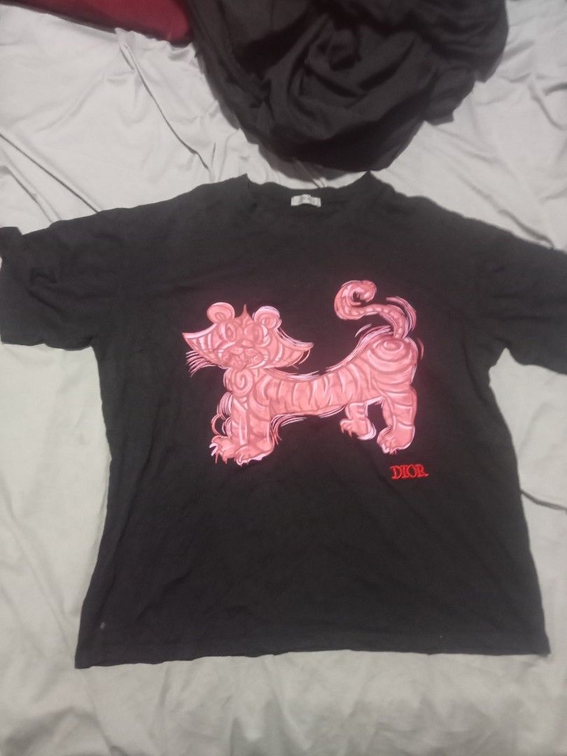 Dior Black Tiger Graphic Tee Size XL (Category: Tshirts & Polo Shirts ) located in Sagay. Submitted by kennie_3377 (Listing ID 1467266281, Image 1). Description: - Brand: Dior - Color: Black - Size: XL (tagged on inside collar) - Design: Pink tiger graphic with red Dior lettering - Material: 100% cotton with embroidery details - Origin: Made in Italy - Condition: Normal wear from past use.