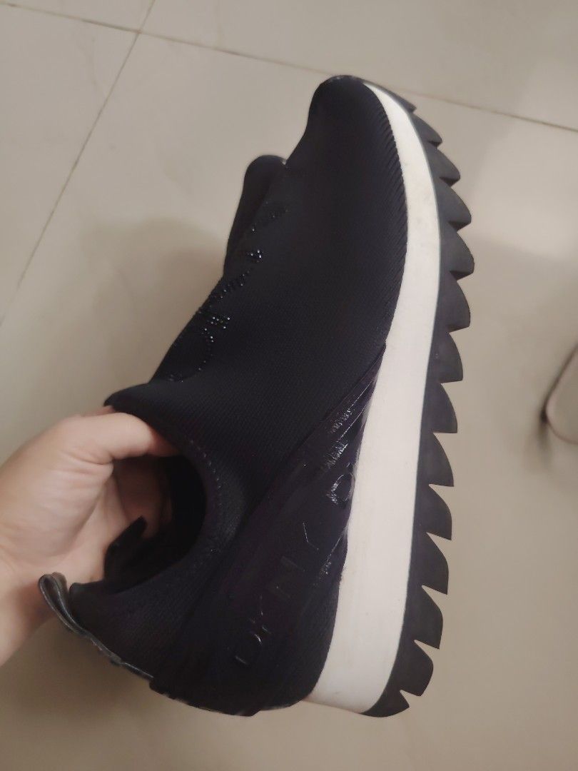 DKNY Black Slip-On Platform Sneakers (Category: Sneakers) located in Tanza. Submitted by kath172 (Listing ID 1467240181, Image 3). Description: - Brand: DKNY - Color: Black with white midsole and black jagged treads - Style: Slip-on sneakers with chunky ridged soles - Material: Stretchy fabric upper - Details: Eye-catching rhinestone DKNY logo lettering down the front - Convenience: Heel pull tab for easy on and off - Condition: Super comfortable