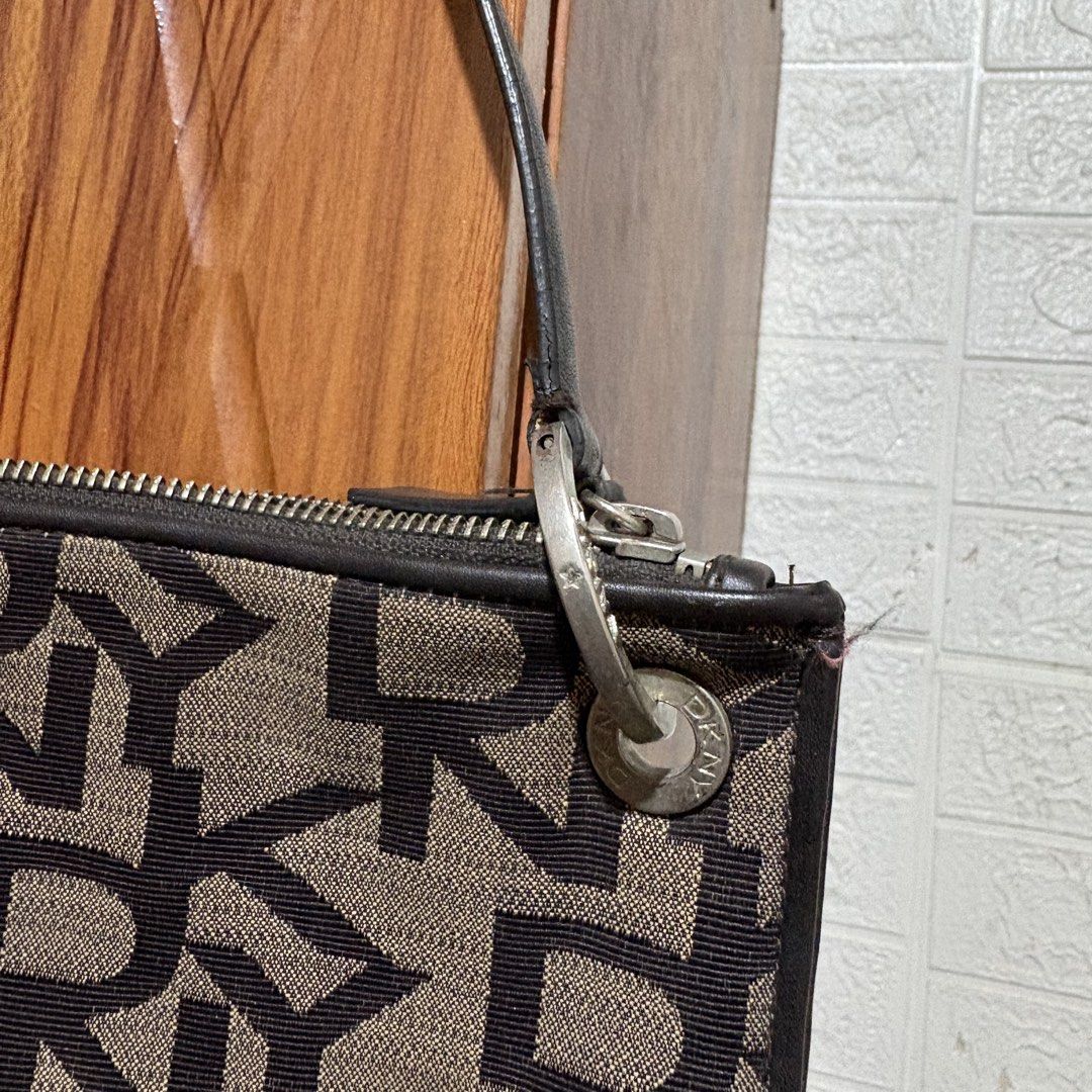 DKNY Monogram Shoulder Bag Brown Black (Category: Luxury Bags & Wallets) located in Carmen. Submitted by rr_thrifts (Listing ID 1467289334, Image 2). Description: - Brand: DKNY - Material: Brown and black monogram canvas with black leather trim - Closure: Top zip closure with leather pull tab - Interior: Beige fabric lining with a zippered pocket and DKNY logo patch - Strap: Single black leather strap with silver-tone hardware - Flaw Notice: Heav