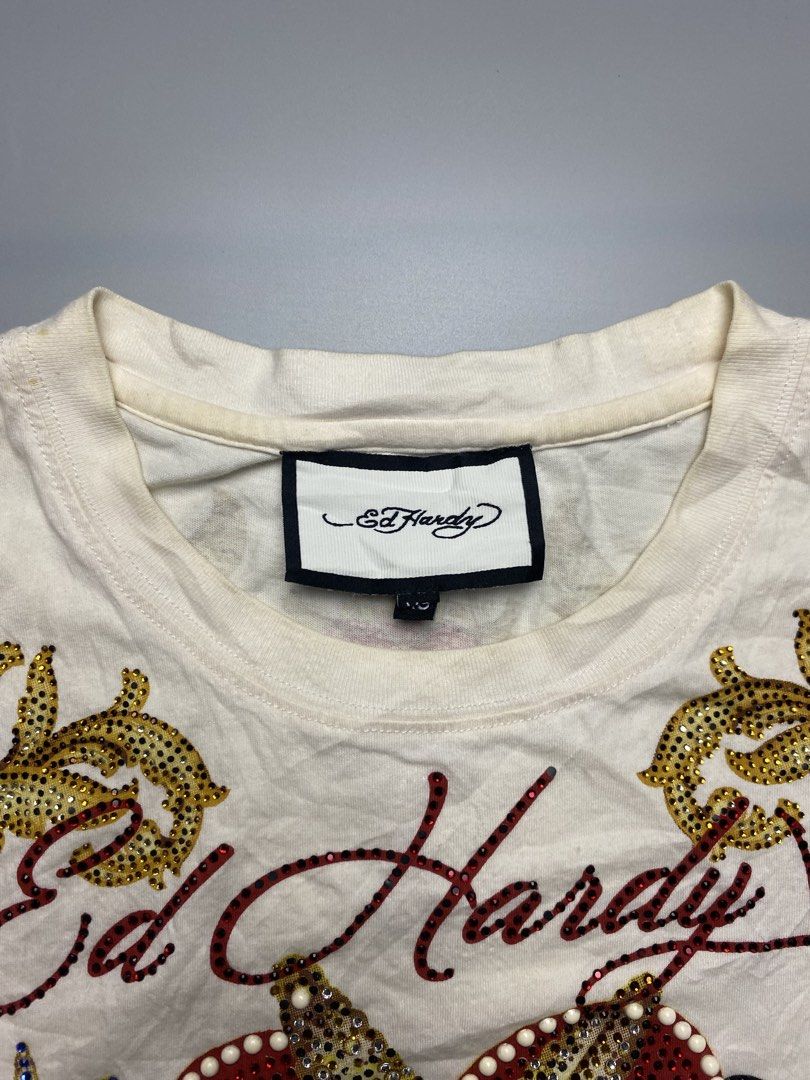 Ed Hardy -Love kills slowly (Category: Tshirts & Polo Shirts ) located in Bacolod City. Submitted by triptothrift_98 (Listing ID 1467169029, Image 3). Description: - Brand: Ed Hardy • Design: “LOVE KILLS SLOWLY” Skull / Heart / Crossbones • Colorway: Cream White x Gold / Red stones • Xs on tag (Best fit medium) • Dimes: 20 width, 27 length • Material: Cotton • Features: All-over rhinestones & studs front + sleeve baroque prints • Condition: Excel