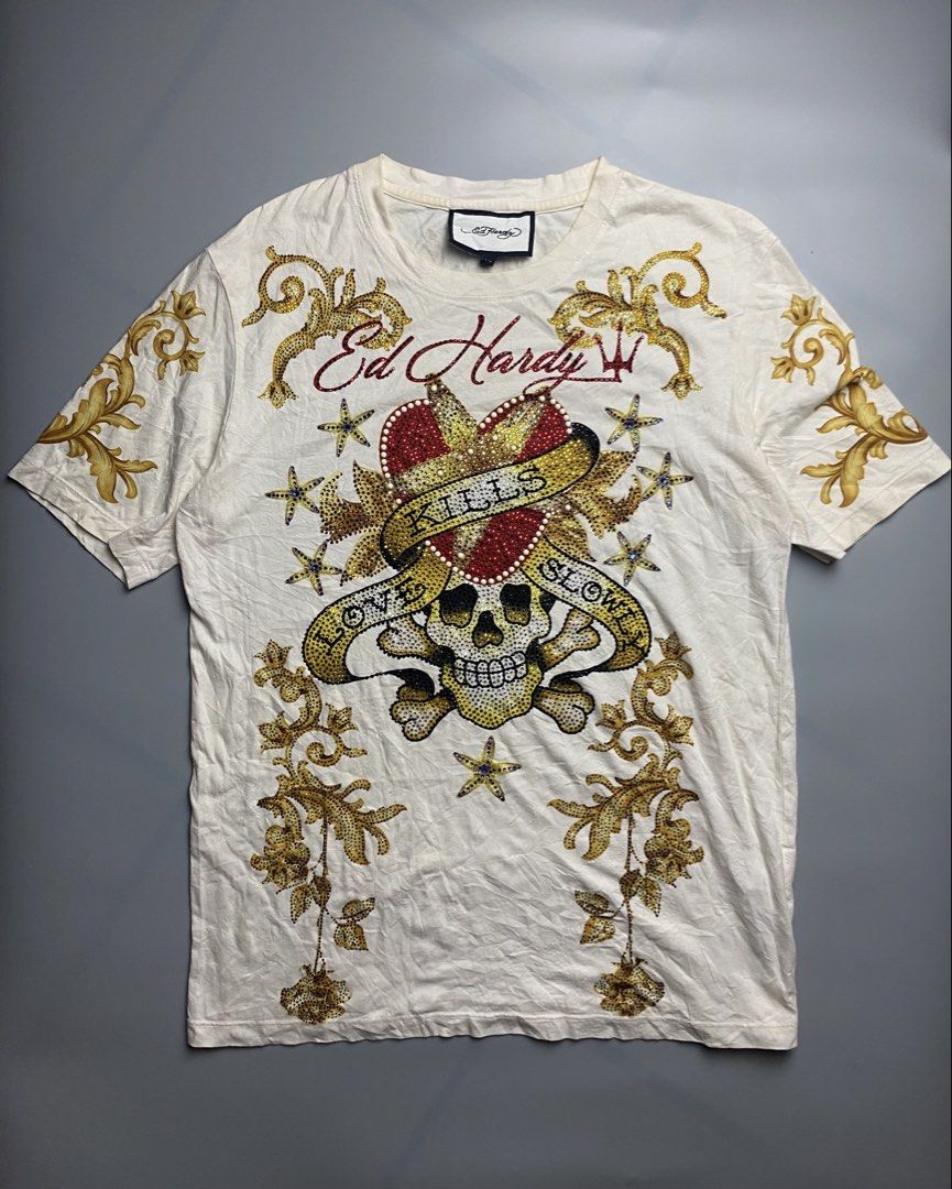 Ed Hardy -Love kills slowly (Category: Tshirts & Polo Shirts ) located in Bacolod City. Submitted by triptothrift_98 (Listing ID 1467169029, Image 1). Description: - Brand: Ed Hardy • Design: “LOVE KILLS SLOWLY” Skull / Heart / Crossbones • Colorway: Cream White x Gold / Red stones • Xs on tag (Best fit medium) • Dimes: 20 width, 27 length • Material: Cotton • Features: All-over rhinestones & studs front + sleeve baroque prints • Condition: Excel