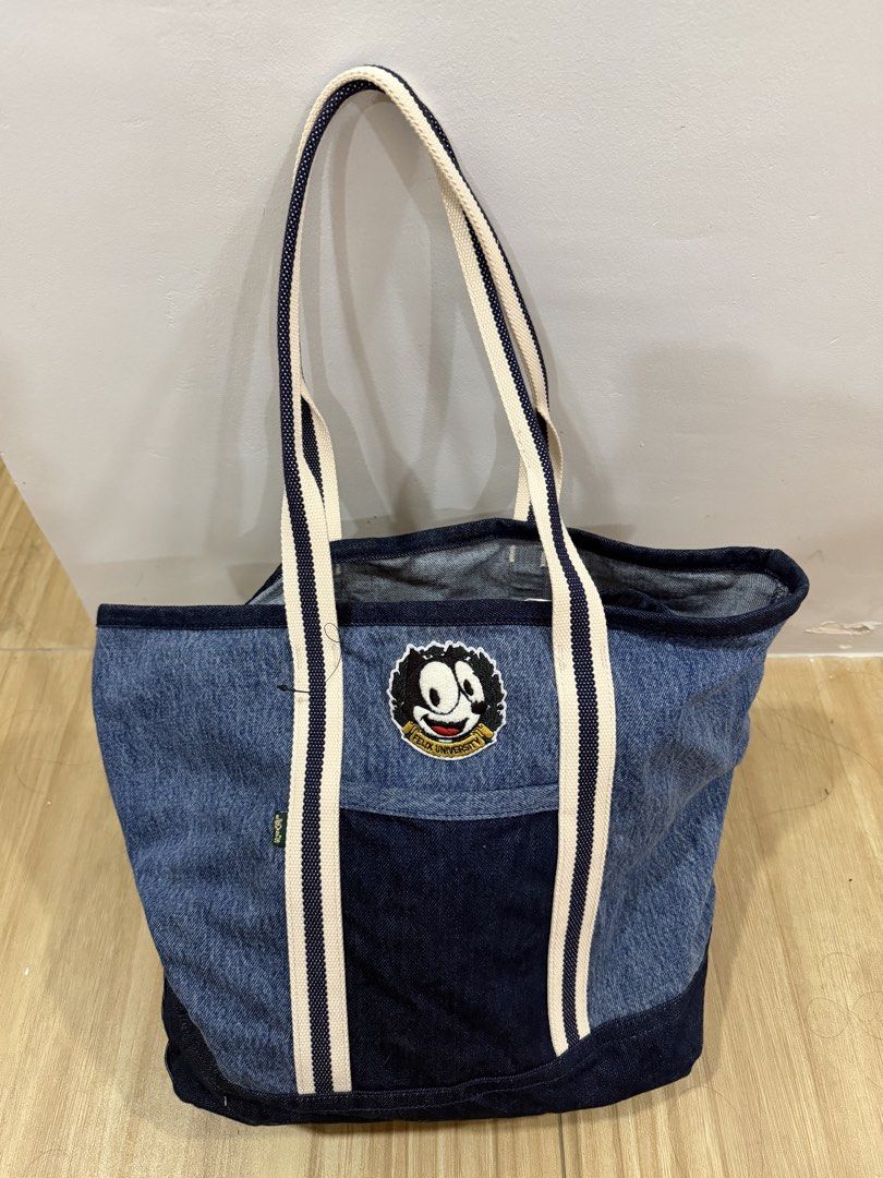 Felix the Cat Denim Tote Bag (Category: Tote Bags) located in Taguig. Submitted by closet.ny (Listing ID 1467189618, Image 1). Description: - Condition: Clean fabric, no major wear - Material: 100% cotton (© 2021 DWA LLC) - Design: Dark denim base and trim with a cool Felix University front pocket patch - Straps: Stylish white and navy striped shoulder straps - Interior: Spacious and practical for everyday essentials RFS: A gift but not used.