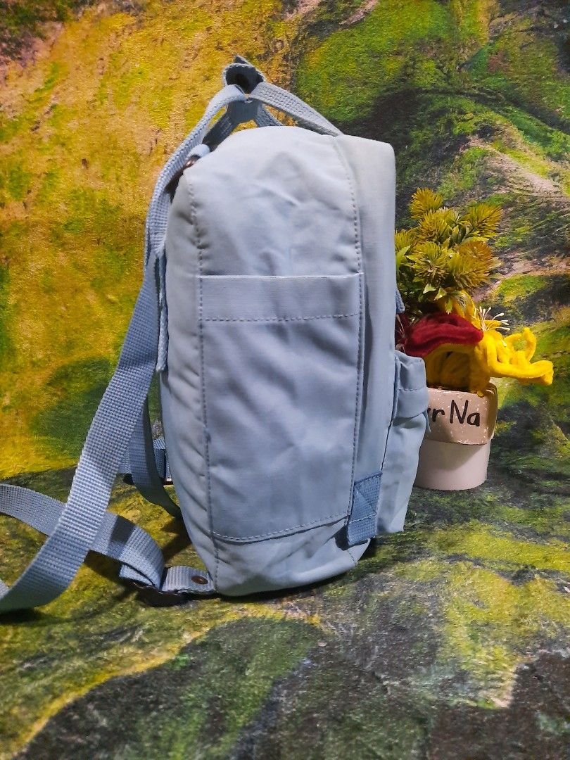 Fjallraven Kanken mini backpack light blue (Category: Backpacks) located in Baguio. Submitted by klayblakeb87803 (Listing ID 1467232541, Image 3). Description: Light blue Fjallraven Kanken mini backpack. Measures 10 inches high by 8 inches base. Front zipper pocket and dual top handles with snap button strap. Adjustable shoulder straps with metal hardware. Round Fjallraven logo patch on front. Shows minor discoloration and dirt marks on the logo 