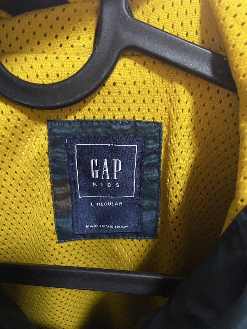 Gap Camo Hooded Jacket Size L Regular (Category: Coats, Jackets and Outerwear) located in Tarlac. Submitted by pangz0918 (Listing ID 1467179843, Image 2). Description: - Brand: Gap Kids - Size: L Regular - Color/Pattern: Dark camouflage with bright yellow mesh lining - Closure: Full zip front - Pockets: Extra zippered chest pocket and lower side pockets - Hood: Attached wind-blocking hood - Material: Lightweight, ideal for school or outdoor play 
