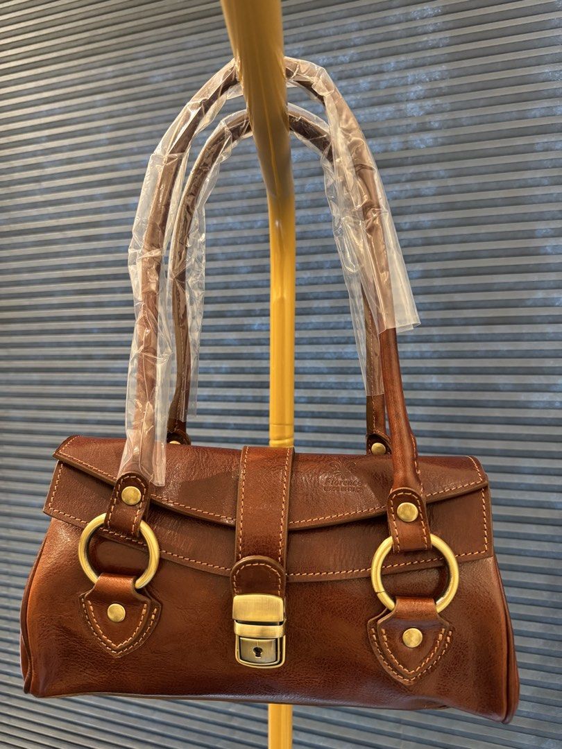 Genuine Italian Leather Handbag Brown (Category: Luxury Bags & Wallets) located in Makati City. Submitted by onlinegaragesale. (Listing ID 1467193019, Image 1). Description: - Authentic brown leather handbag - Dimensions: 27 x 15 x 9 cm - Structured design with dual shoulder straps - Chic metallic ring hardware and metal lock closure - Convenient front flap pockets with contrast stitching - Clean and spacious interior compartment.