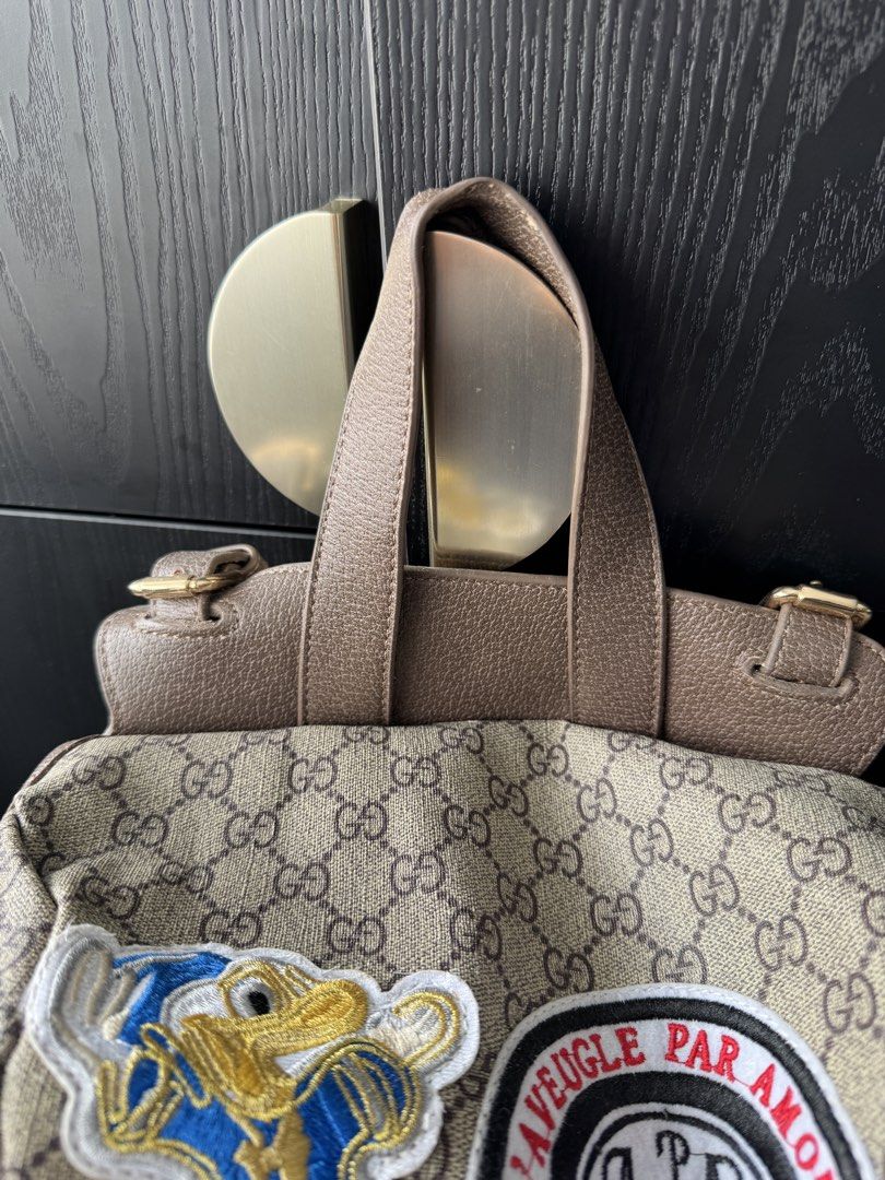Canvas Patchwork Backpack (Category: Backpacks) located in Singapore. Submitted by rehomeedit (Listing ID 1467262238, Image 7). Description: - Backpack in iconic canvas - Features fun embroidered patches including a tiger, flowers, and Donald Duck - Brown leather trim and adjustable straps - Secure drawstring top closure with a buckle flap - Convenient side pockets with flap closures and snap buttons - Accented with the signature green and red We