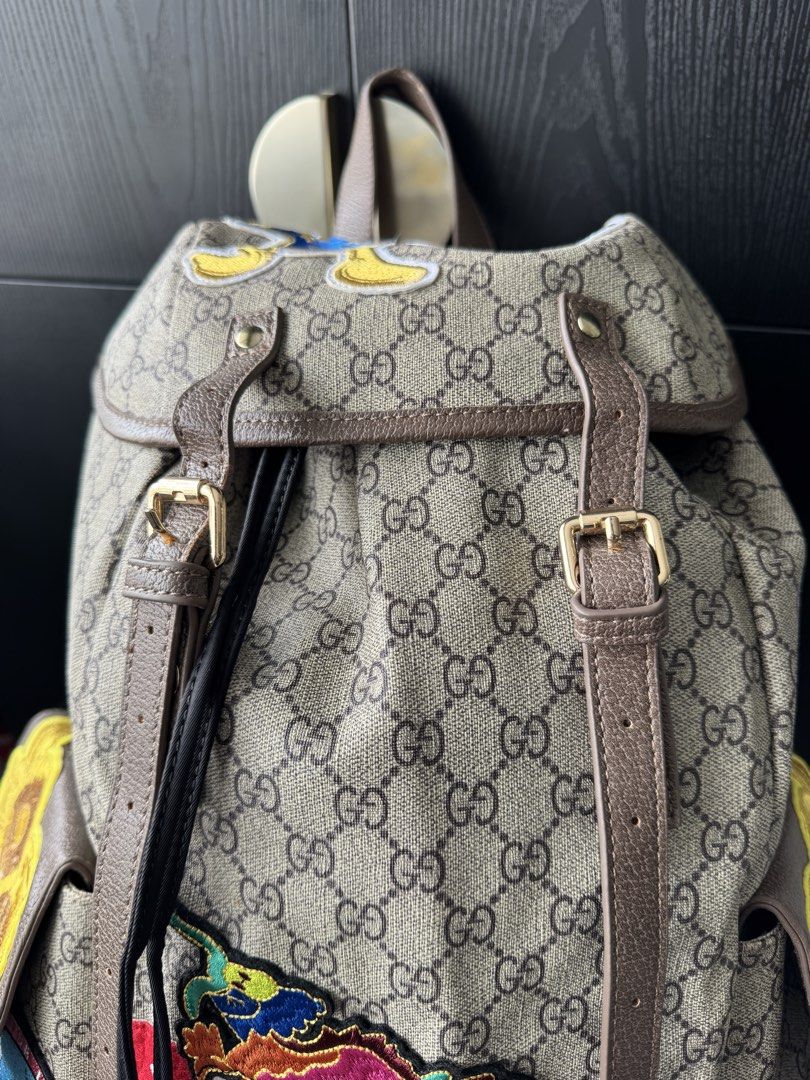Canvas Patchwork Backpack (Category: Backpacks) located in Singapore. Submitted by rehomeedit (Listing ID 1467262238, Image 6). Description: - Backpack in iconic canvas - Features fun embroidered patches including a tiger, flowers, and Donald Duck - Brown leather trim and adjustable straps - Secure drawstring top closure with a buckle flap - Convenient side pockets with flap closures and snap buttons - Accented with the signature green and red We