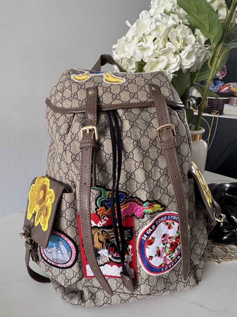 Canvas Patchwork Backpack (Category: Backpacks) located in Singapore. Submitted by rehomeedit (Listing ID 1467262238, Image 1). Description: - Backpack in iconic canvas - Features fun embroidered patches including a tiger, flowers, and Donald Duck - Brown leather trim and adjustable straps - Secure drawstring top closure with a buckle flap - Convenient side pockets with flap closures and snap buttons - Accented with the signature green and red We