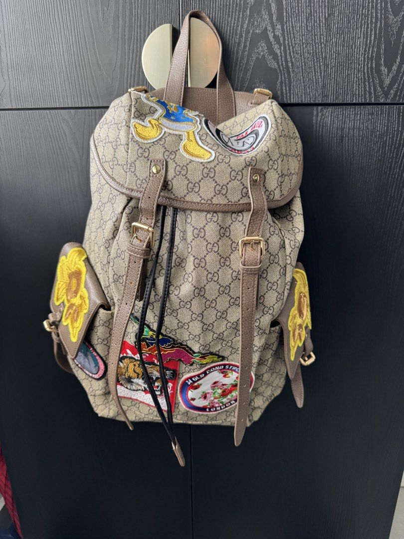 Canvas Patchwork Backpack (Category: Backpacks) located in Singapore. Submitted by rehomeedit (Listing ID 1467262238, Image 5). Description: - Backpack in iconic canvas - Features fun embroidered patches including a tiger, flowers, and Donald Duck - Brown leather trim and adjustable straps - Secure drawstring top closure with a buckle flap - Convenient side pockets with flap closures and snap buttons - Accented with the signature green and red We