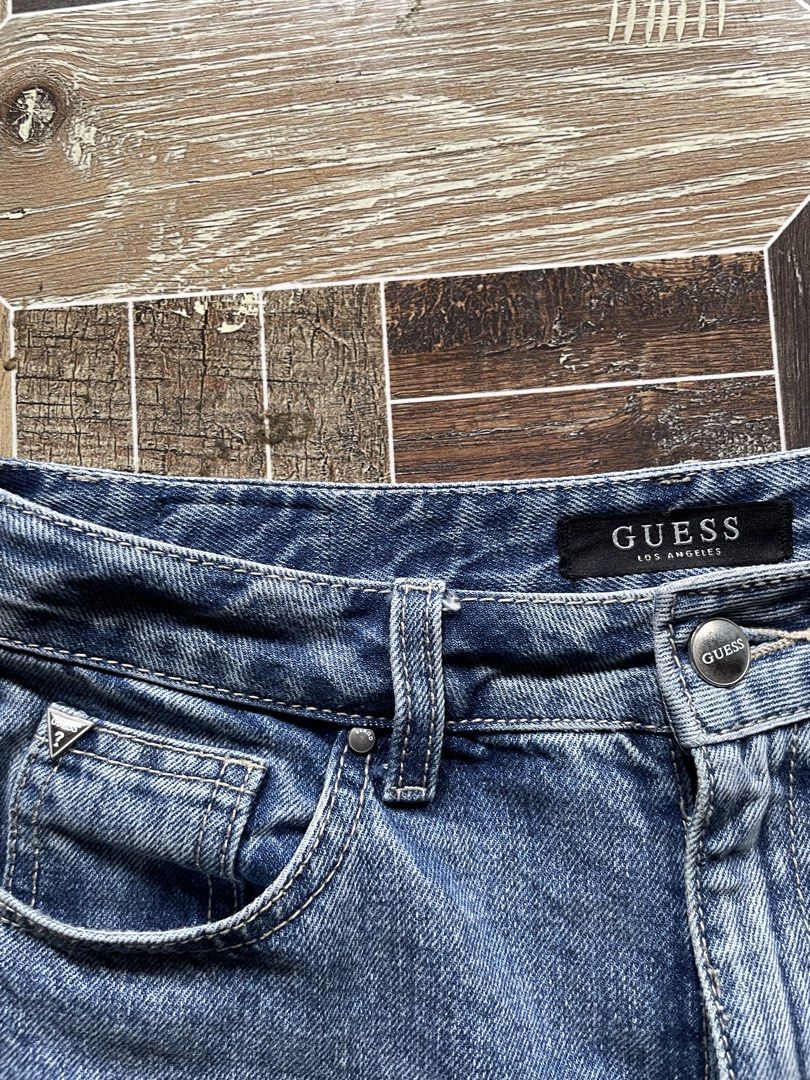 Guess Los Angeles Denim Shorts (Category: Jeans) located in Davao. Submitted by vin.my (Listing ID 1467202807, Image 2). Description: Guess denim shorts in mid-blue wash. High-waisted style with front button and zipper closure. Classic five-pocket layout including coin pocket with metal triangle logo. Back pocket features silver Guess triangle plaque and brown leather logo patch on the waistband. Heavy stonewash finish with traditional contrast s