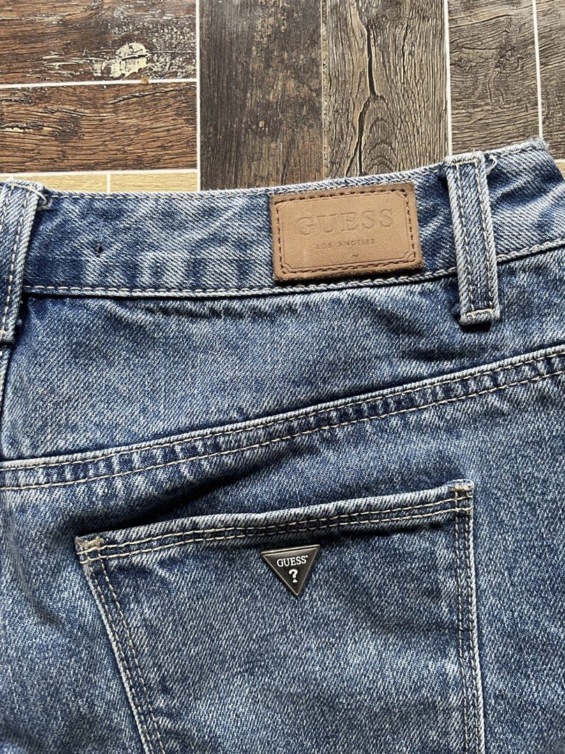 Guess Los Angeles Denim Shorts (Category: Jeans) located in Davao. Submitted by vin.my (Listing ID 1467202807, Image 3). Description: Guess denim shorts in mid-blue wash. High-waisted style with front button and zipper closure. Classic five-pocket layout including coin pocket with metal triangle logo. Back pocket features silver Guess triangle plaque and brown leather logo patch on the waistband. Heavy stonewash finish with traditional contrast s