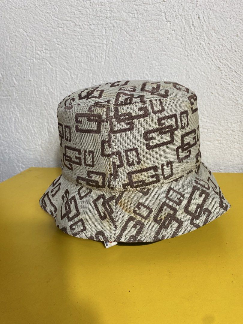 Guess Monogram Pattern Beige And Brown Bucket Hat (Category: Hats & Beanies) located in Cabanatuan. Submitted by brightwater-2083 (Listing ID 1465955153, Image 2). Description: - Beige bucket hat with all-over brown monogram pattern - Features a stylish dark brown leather-like accent tab near the brim - Fully lined with light beige fabric on the interior - Flaw note: Shows visible yellowish stains around the lower brim and seam area as pictured -