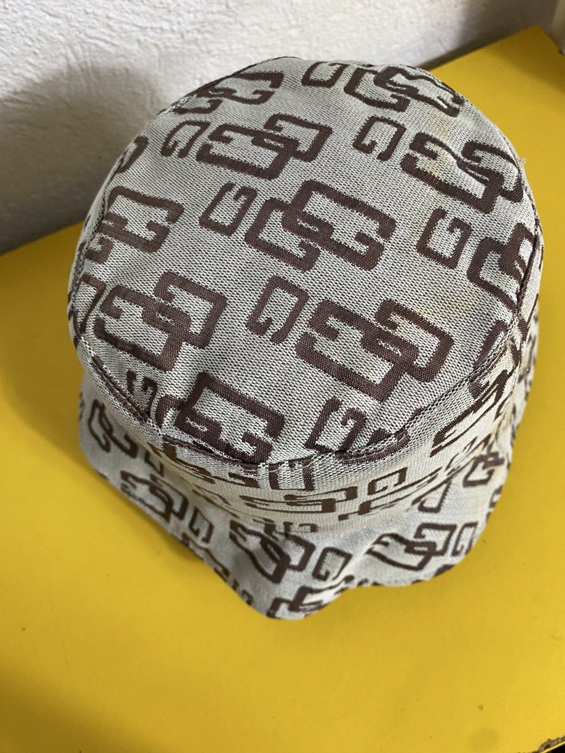 Guess Monogram Pattern Beige And Brown Bucket Hat (Category: Hats & Beanies) located in Cabanatuan. Submitted by brightwater-2083 (Listing ID 1465955153, Image 3). Description: - Beige bucket hat with all-over brown monogram pattern - Features a stylish dark brown leather-like accent tab near the brim - Fully lined with light beige fabric on the interior - Flaw note: Shows visible yellowish stains around the lower brim and seam area as pictured -