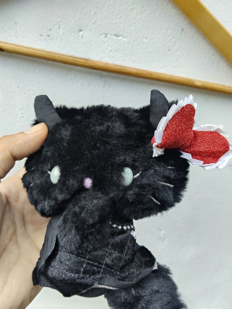 Hello Kitty Black Devil Black goth plush toy with red bow (Category: Plushies & Soft Toys) located in City of Isabela. Submitted by jasheverything (Listing ID 1467351195, Image 2). Description: - Adorable black plush cat toy with a soft furry texture - Features cute devil horns and sparkling red bow with white trim - Wears a dark velvet dress with a silver heart pendant design - Compact and easy to hold (great for all ages) - Perfect gift for cat