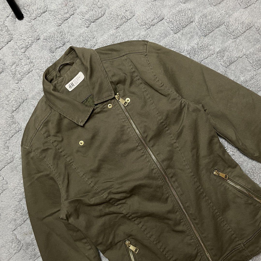H&M Olive Green Biker Jacket (Category: Coats, Jackets and Outerwear) located in Tarlac. Submitted by thriftspot2024 (Listing ID 1467282293, Image 2). Description: Olive green utility jacket from H&M. Asymmetrical front zip closure with gold-tone hardware and snap button collar. Two zippered side pockets and structured stitching details throughout. Made from cotton blend material with polyester lining. Tagged size EUR 170 / US 14Y+, fits like a w