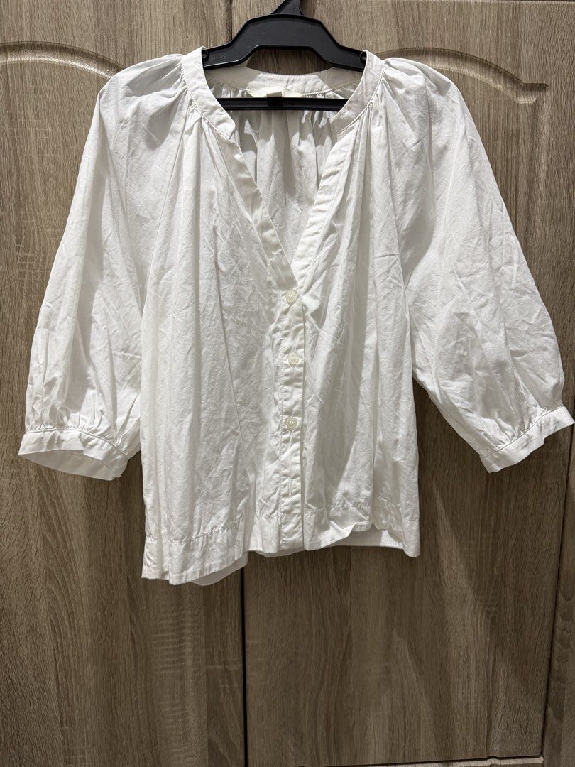 H&M White Long Sleeves Deep V-Neck (Category: Blouses) located in Calamba. Submitted by nicalison (Listing ID 1467310966, Image 1). Description: - Brand: H&M - Size: XS (EUR/US sizing) - Color: Classic White - Design: V-neck collar with button-down front - Sleeves: Three-quarter puff sleeves with gathered cuffs - Fit: Relaxed, lightweight cotton material - Style: Minimalist basic, easy to pair with jeans or skirts for everyday wear.