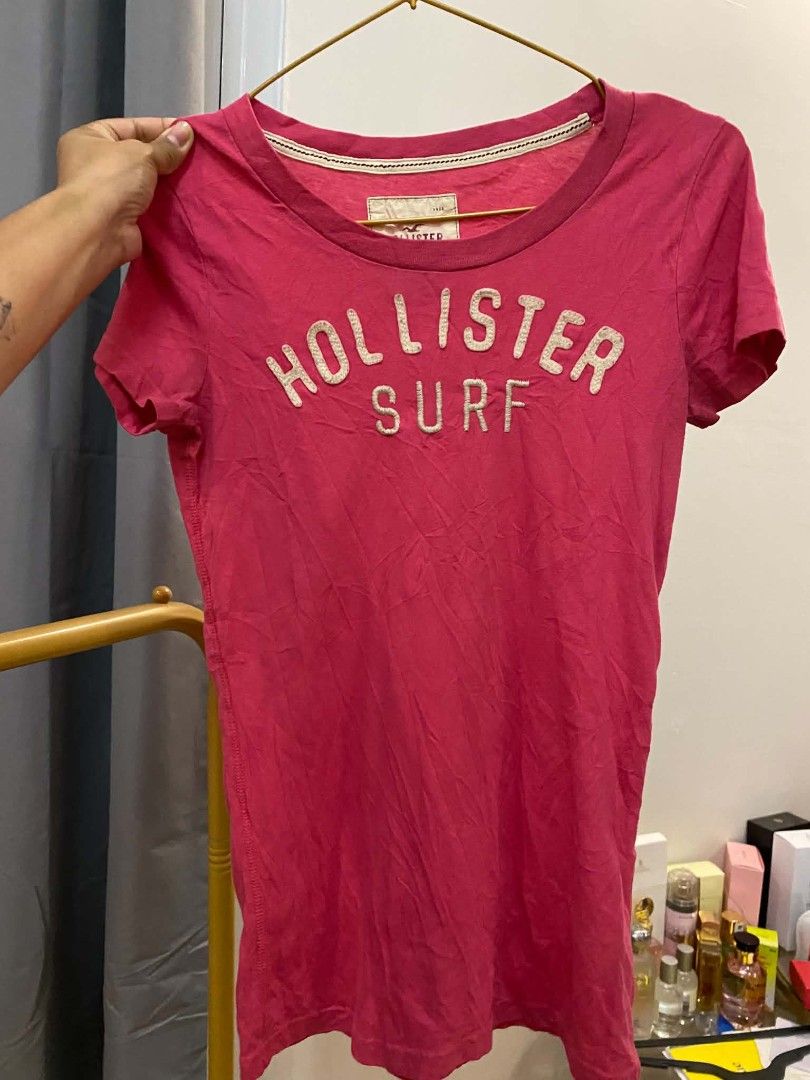 Hollister Surf Pink Graphic Tee (Category: Activewear) located in Malasiqui. Submitted by finnley26 (Listing ID 1467244344, Image 2). Description: - Brand: Hollister - Color: Bright pink with white textured chest lettering - Style: Short sleeves, scoop neck, casual everyday top - Condition: Good, has normal storage creasing and needs a quick iron.