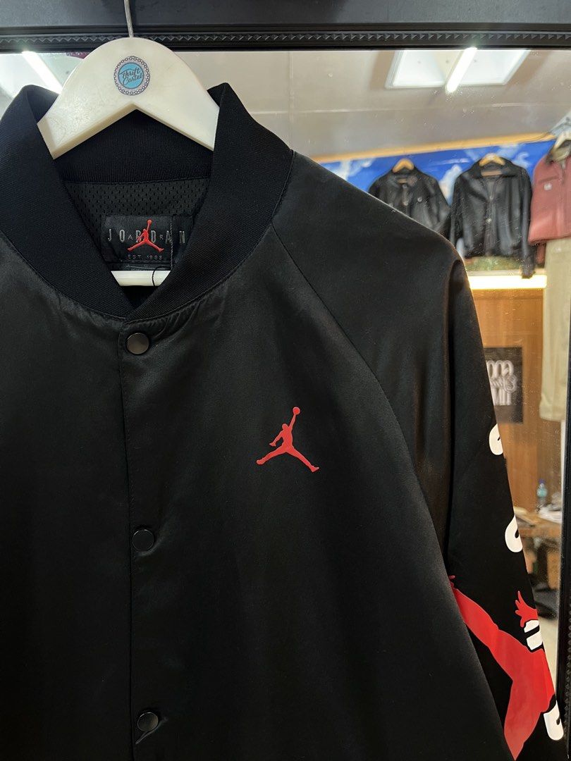Jordan Black Satin Bomber Jacket (Category: Coats, Jackets and Outerwear) located in Baguio. Submitted by thrash2cash_2600 (Listing ID 1467264335, Image 2). Description: - Brand: Jordan - Color: Black with red details - Material: Satin with breathable mesh lining - Size: Large - Design: Embroidered chest Jumpman logo, sleeve graphic print - Features: Snap-button closure, two front pockets, ribbed collar, cuffs, and hem.