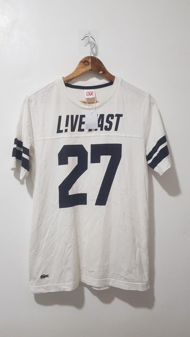 Lacoste Live T-shirt Number 27 White (Category: Shirts) located in Manila. Submitted by nice430 (Listing ID 1467296313, Image 1). Description: - Brand: Lacoste Live - Color: White with navy blue sleeve stripes - Size: 2 (95cm chest measurement) - Material: 100% Cotton - Design: Crew neck with contrast collar trim, front 'Live Fast 27' print, and signature crocodile logo patch near the hem - Condition: Brand new with original neck tag and interior