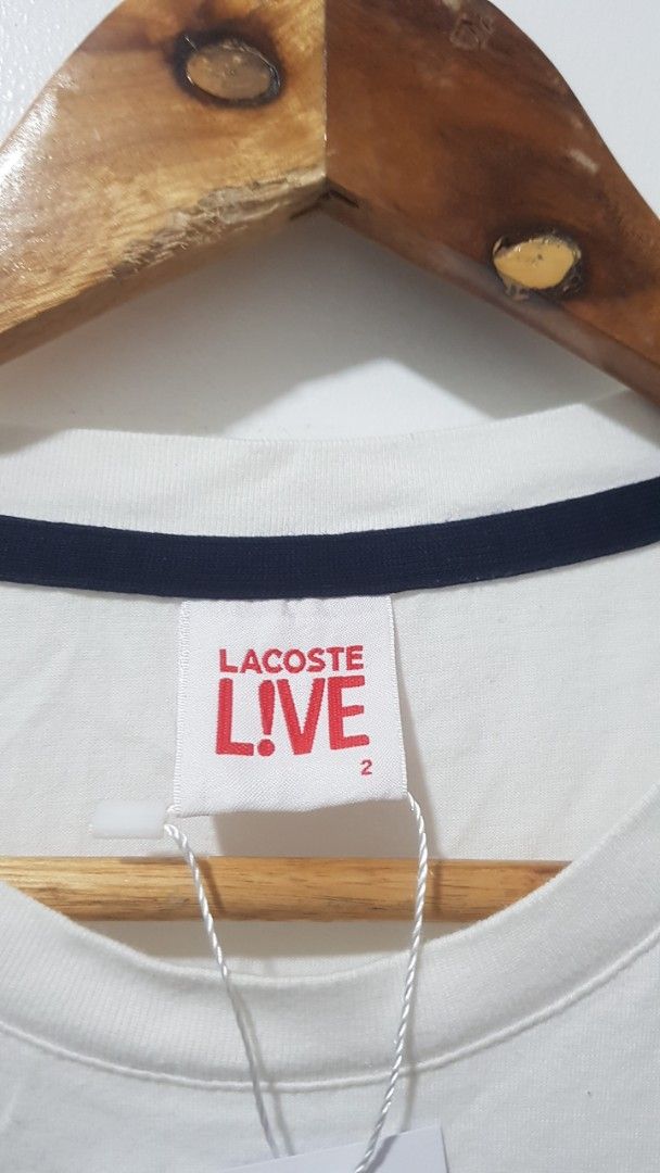Lacoste Live T-shirt Number 27 White (Category: Shirts) located in Manila. Submitted by nice430 (Listing ID 1467296313, Image 3). Description: - Brand: Lacoste Live - Color: White with navy blue sleeve stripes - Size: 2 (95cm chest measurement) - Material: 100% Cotton - Design: Crew neck with contrast collar trim, front 'Live Fast 27' print, and signature crocodile logo patch near the hem - Condition: Brand new with original neck tag and interior
