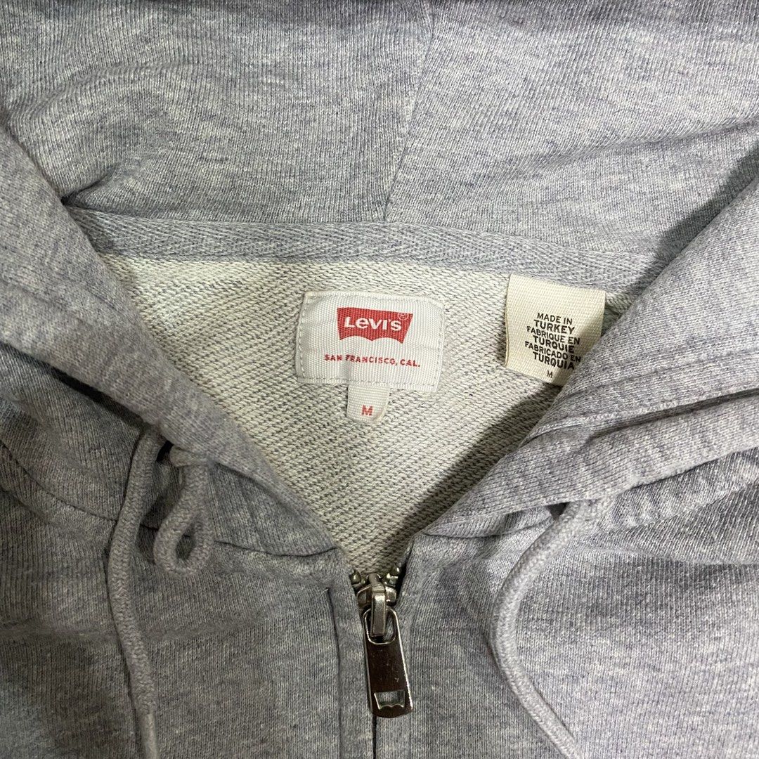 Levi's Grey Zip-Up Hoodie with Script Logo (Category: Hoodies) located in Loreto, Surigao del Norte. Submitted by ongcollection_747 (Listing ID 1467329958, Image 2). Description: - Brand: Levi's - Item: Zip-up hoodie - Size: Medium - Color: Grey with red and blue script logo - Features: Full zipper front, adjustable hood drawstrings, front kangaroo pockets, and classic red tab on the cuff - Condition: Clean fleece material inside and out.