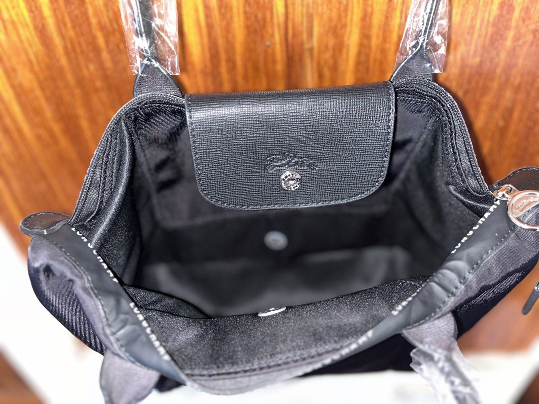 Longchamp Black Tote Bag with Top Handles (Category: Tote Bags) located in Lucena. Submitted by unnieskollegsyeononlineshop (Listing ID 1467315876, Image 3). Description: - Color: Classic Black - Condition: Brand new, handles still in original plastic packaging with brand tag attached - Closure: Leather flap snap closure and secure zippered top with a pull cord - Exterior: Longchamp lettering printed along the upper fabric trim - Interior: Clean 