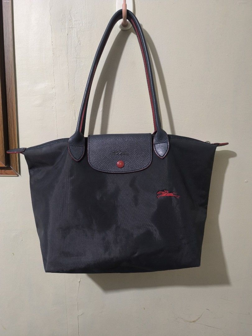 Longchamp Le Pliage Shoulder Tote Bag Navy (Category: Luxury Bags & Wallets) located in Bay. Submitted by alegnaacir (Listing ID 1467189764, Image 1). Description: - Color: Dark navy blue with red details -Size: Medium - Material: Durable nylon - Straps: Long shoulder handles with red edging - Closure: Flap closure with embossed horse logo and red button snap - Branding: Red embroidered horse emblem on lower front - Condition: Clean corner seams 