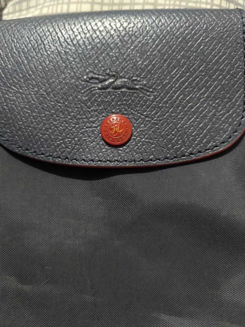 Longchamp Le Pliage Shoulder Tote Bag Navy (Category: Luxury Bags & Wallets) located in Bay. Submitted by alegnaacir (Listing ID 1467189764, Image 2). Description: - Color: Dark navy blue with red details -Size: Medium - Material: Durable nylon - Straps: Long shoulder handles with red edging - Closure: Flap closure with embossed horse logo and red button snap - Branding: Red embroidered horse emblem on lower front - Condition: Clean corner seams 