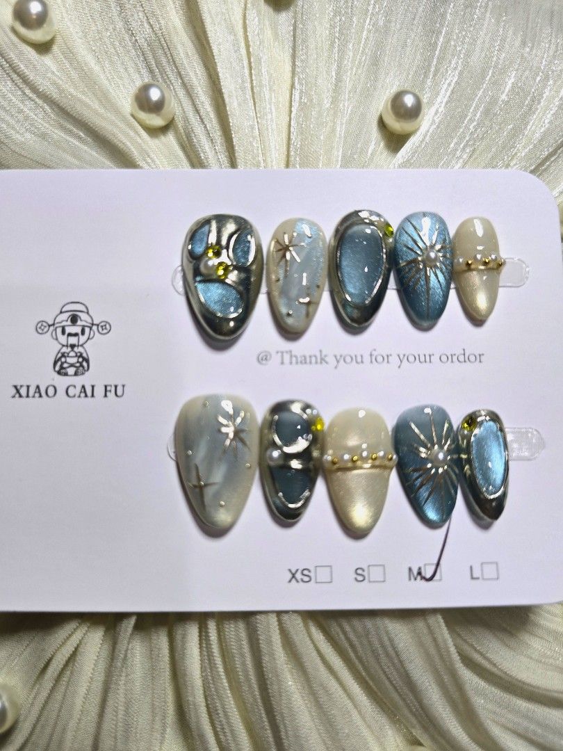 Medium Short Almond Blue and silver celestial press-on nail set (Category: Hands & Nails) located in Makati City. Submitted by jangmiscloset (Listing ID 1467315967, Image 1). Description: Double the glam, get a bonus! Buy any 2 sets (₱200 and up ) and receive a ₱100 nail set FREE. Mix & match your faves and enjoy more styles without spending extra ✨Design: Blue and cream shades with celestial star details, rhinestones, pearl accents, and metallic