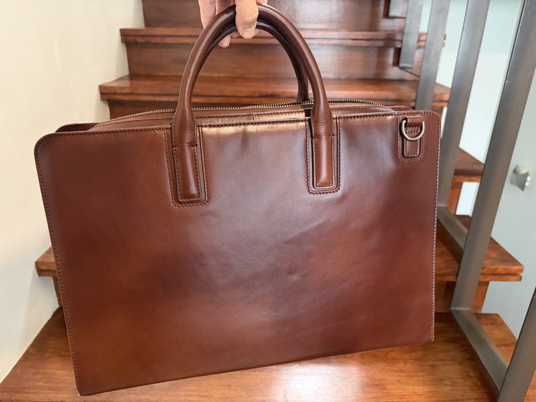 Motherhouse Brown Leather Briefcase Work Bag (Category: Briefcases) located in Taguig. Submitted by ellejay8 (Listing ID 1467245102, Image 2). Description: - Brand/Model: Motherhouse leather briefcase - Color: Rich brown - Material: Sturdy leather with structured silhouette - Interior: Striped fabric lining, multiple compartments, zipped pockets, and pen holders - Closure: Secure main zip closure - Extra Feature: Metal ring attachment on the side