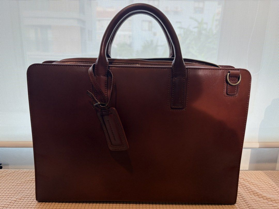 Motherhouse Brown Leather Briefcase Work Bag (Category: Briefcases) located in Taguig. Submitted by ellejay8 (Listing ID 1467245102, Image 1). Description: - Brand/Model: Motherhouse leather briefcase - Color: Rich brown - Material: Sturdy leather with structured silhouette - Interior: Striped fabric lining, multiple compartments, zipped pockets, and pen holders - Closure: Secure main zip closure - Extra Feature: Metal ring attachment on the side