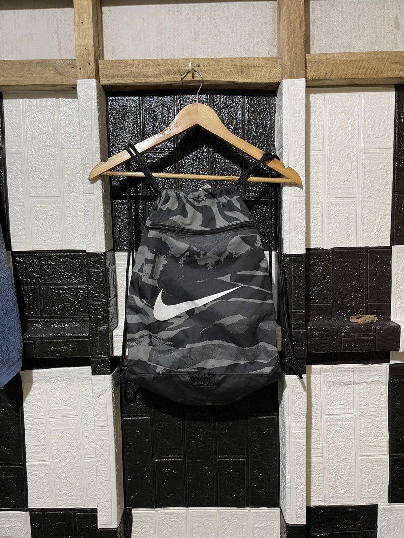 Nike Camo Gym Sack Drawstring Bag (Category: Backpacks) located in Lopez. Submitted by thrift.ni.roms22 (Listing ID 1467168273, Image 1). Description: - Brand: Nike - Item: Drawstring Gym Sack / Bag - Color/Pattern: Grey and Black Camo - Design: Large white Nike Swoosh logo on front - Storage: Front zippered pocket with Nike branded pull - Closure: Secure top drawstring - Material: 100% Polyester (Made in Indonesia) - Product Code: CU9646 010 - C