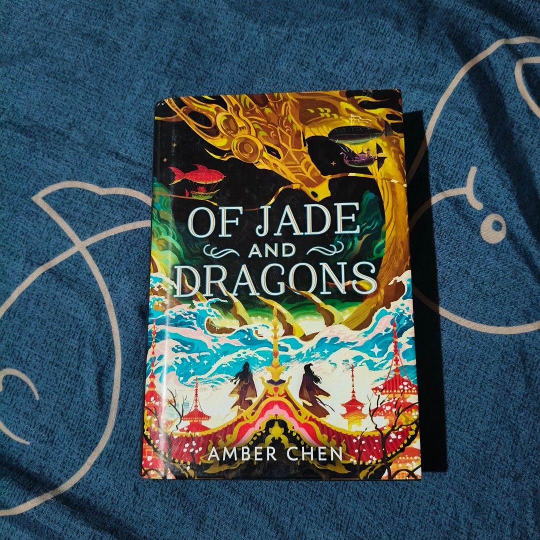 Of Jade and Dragons by Amber Chen (Category: Storybooks) located in Villasis. Submitted by rajjinni (Listing ID 1467297368, Image 1). Description: - Title: Of Jade and Dragons - Author: Amber Chen - Format: Hardcover with gorgeous golden dragon cover art - Condition: Read once, well-maintained, and kept on shelf; inside pages are clean and white - Perfect read for fantasy book lovers.