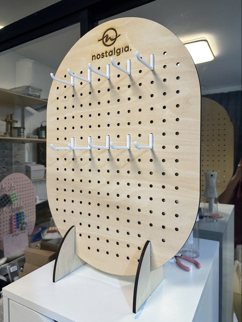 Personalized Wooden Pegboard Display Stand with Hooks (Category: Shelves, Cabinets & Racks) located in Malolos. Submitted by jelikaaaaa (Listing ID 1467253171, Image 2). Description: - Brand: Nostalgia - Design: Oval wooden pegboard with natural finish and laser-etched logo - Included: Removable wooden base support stands and white metal hooks - Versatile: Multiple pre-drilled holes for hanging items - Ideal Use: Perfect for craft fairs, retail d