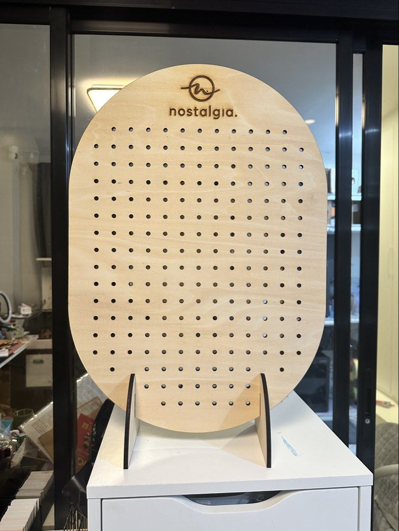 Personalized Wooden Pegboard Display Stand with Hooks (Category: Shelves, Cabinets & Racks) located in Malolos. Submitted by jelikaaaaa (Listing ID 1467253171, Image 3). Description: - Brand: Nostalgia - Design: Oval wooden pegboard with natural finish and laser-etched logo - Included: Removable wooden base support stands and white metal hooks - Versatile: Multiple pre-drilled holes for hanging items - Ideal Use: Perfect for craft fairs, retail d