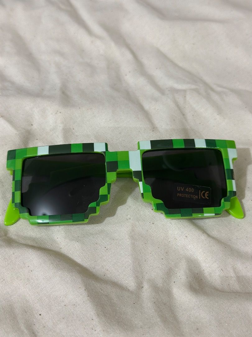 Pixelated Minecraft Green Sunglasses UV400 Protection (Category: Babies & Kids Fashion) located in Mandaluyong City. Submitted by lovedbyjaaaam (Listing ID 1467276791, Image 1). Description: - Product: Green Pixelated Gamer Sunglasses - Lenses: Black lenses with UV400 protection sticker still attached - Frame: Lightweight plastic with a green pixel grid pattern - Best For: Gaming fans, parties, cosplay, and novelty wear - Condition: Brand new, ex