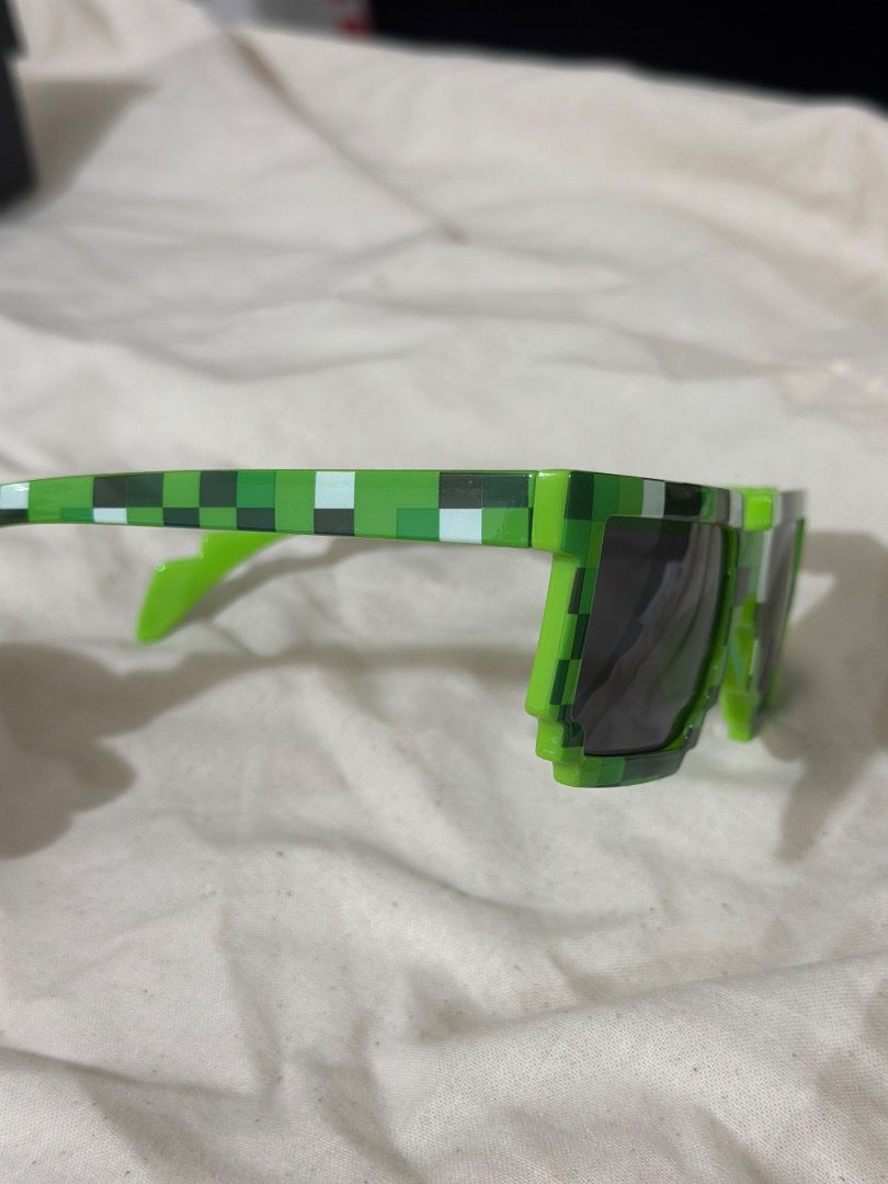 Pixelated Minecraft Green Sunglasses UV400 Protection (Category: Babies & Kids Fashion) located in Mandaluyong City. Submitted by lovedbyjaaaam (Listing ID 1467276791, Image 3). Description: - Product: Green Pixelated Gamer Sunglasses - Lenses: Black lenses with UV400 protection sticker still attached - Frame: Lightweight plastic with a green pixel grid pattern - Best For: Gaming fans, parties, cosplay, and novelty wear - Condition: Brand new, ex