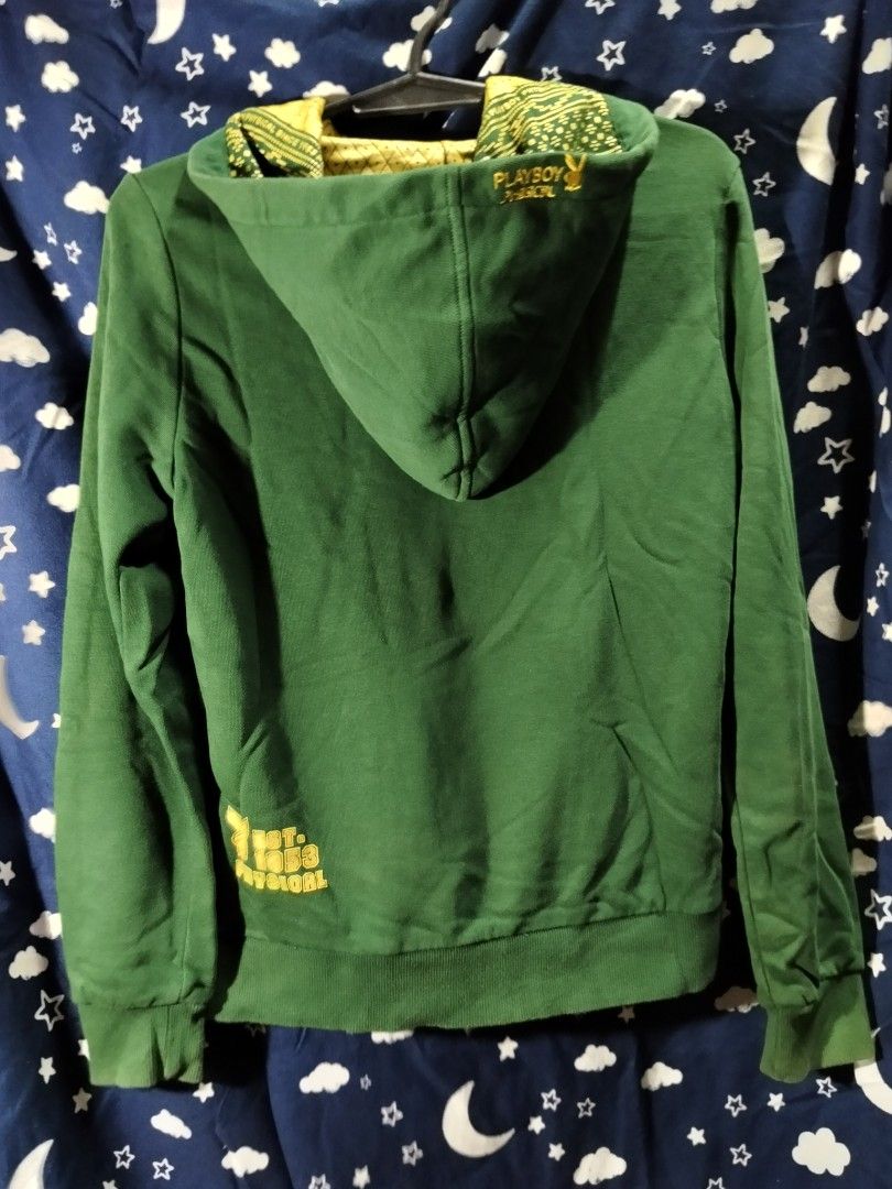 Playboy Physical Green Hoodie (Category: Coats, Jackets and Outerwear) located in Manila. Submitted by tawnycollectiblesshop (Listing ID 1467218930, Image 3). Description: - Size: Fits Medium - Color: Green with contrasting yellow patterned hood lining - Design: Large front graphic print with '53' and Playboy branding, plus extra logo detail on the lower back - Features: Practical kangaroo pocket, ribbed cuffs, and hem - Condition: Pre-loved, wel