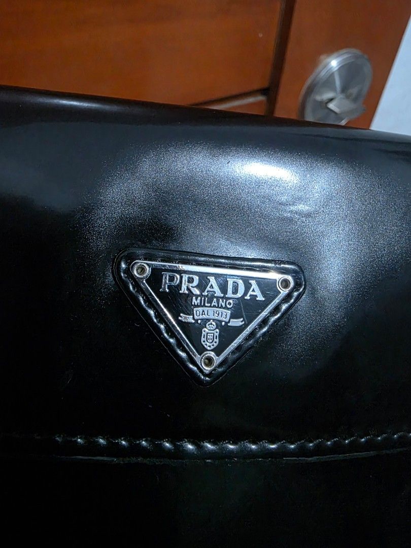 Prada Black Patent Leather Shoulder Bag (Category: Luxury Bags & Wallets) located in Lemery. Submitted by venus23 (Listing ID 1467191129, Image 2). Description: - Brand: Prada - Material: Black patent leather with glossy finish - Hardware & Logo: Silver-tone hardware with classic triangle logo plaque - Closure: Flap closure - Interior: Clean dark lining with enough room for daily essentials - Condition: Excellent/Classic piece.